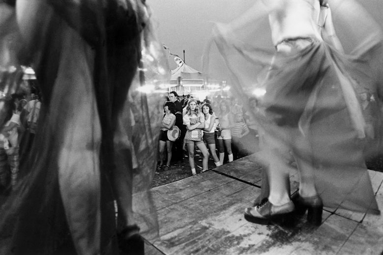 Dancers on the stage while onlookers from the audience watch their skirts twirl. 